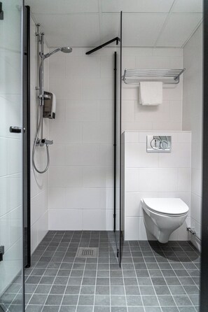 A modern bathroom with a glass shower enclosure, a white toilet, and a towel rack. - Hotelli Sointu (Jarvenpaa)