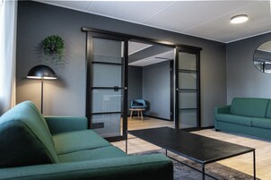 Un espacio de oficina moderno con un sofá verde, una mesa de centro, una lámpara y un puerta corrediza de vidrio que da a otra habitación.