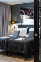 Habitación de hotel con una cama doble, ropa de cama gris, un cabecero con una imagen y una cortina gris.