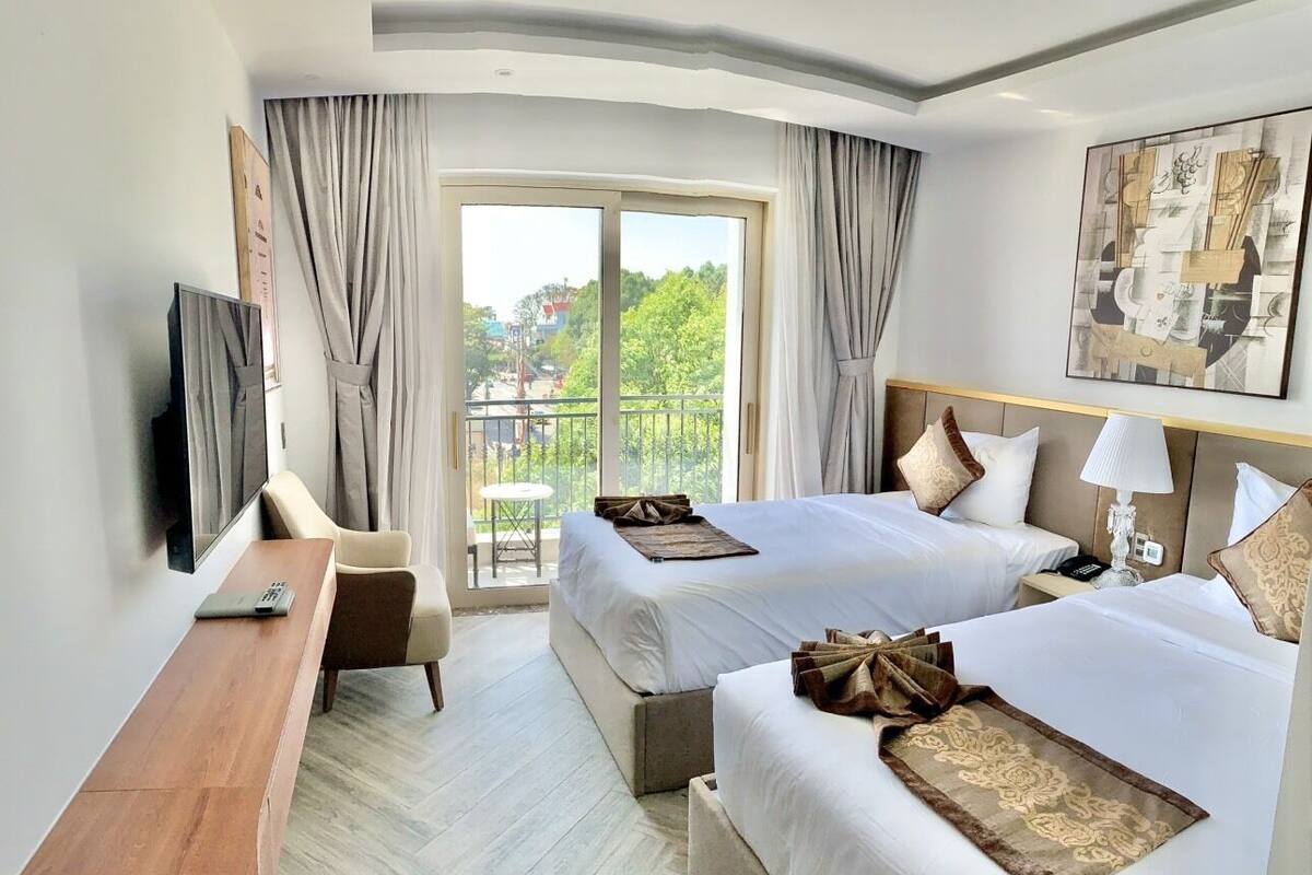 Ein Hotelzimmer mit zwei Betten, einem Schreibtisch, einem Fernseher und einem Balkon mit Blick.