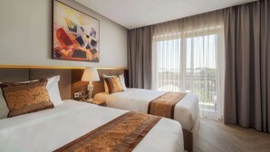 Ein Hotelzimmer mit zwei Betten, einem großen Fenster mit Vorhängen, einem Wandbild und einem Nachttisch mit einer Lampe.