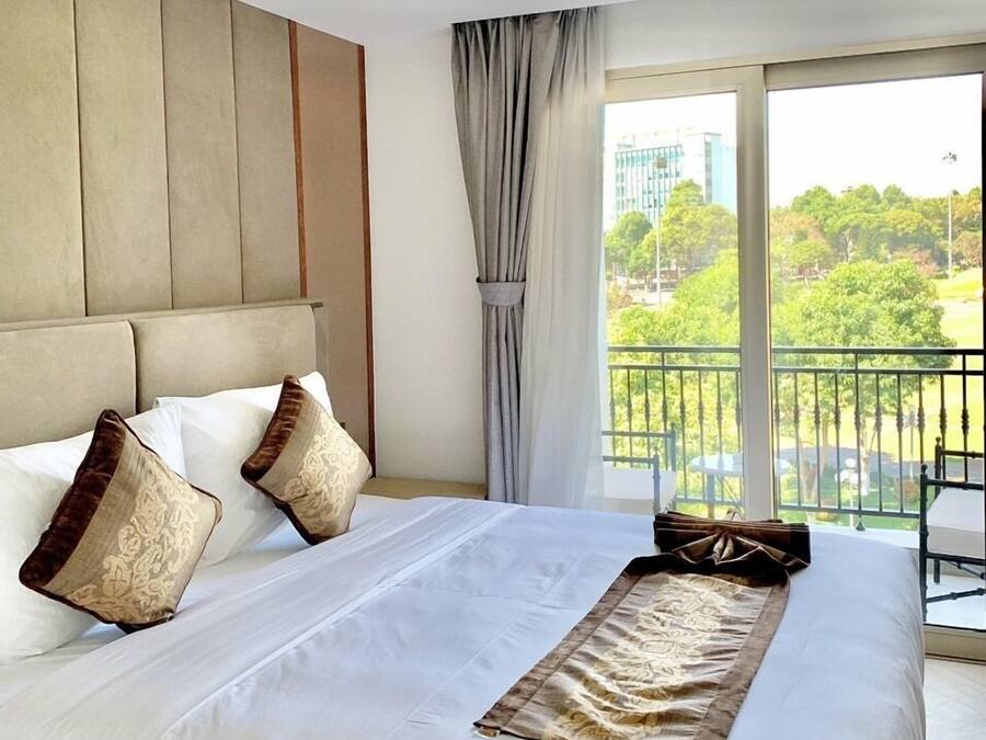 A hotel room with a large bed, a headboard, and a view of a balcony with greenery.