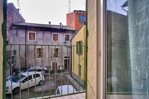 A courtyard with a green metal gate, a white car, and a yellow building with a red roof.