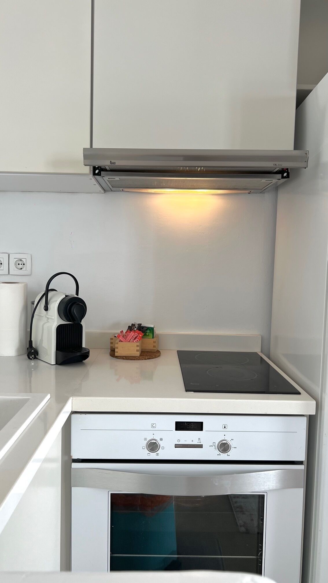 A compact kitchen with a built-in oven, a stovetop, and a microwave. There is a small countertop with a kettle and a box of tea bags.