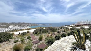 Eine Küstenlandschaft mit Blick auf das Meer, weißen Gebäuden und einem Garten mit Kakteen und Sträuchern.