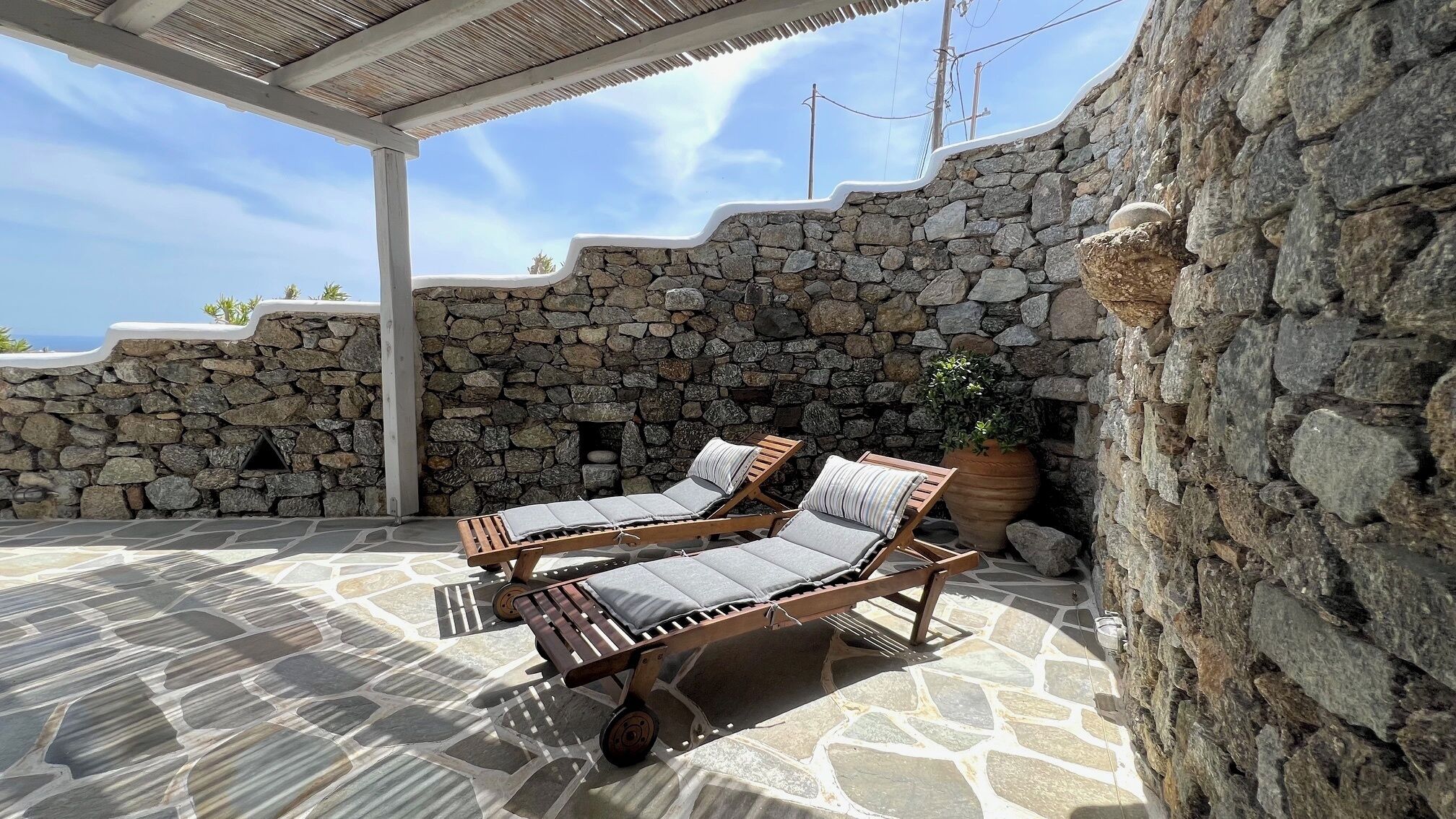 A stone-walled outdoor seating area with two lounge chairs and a potted plant.