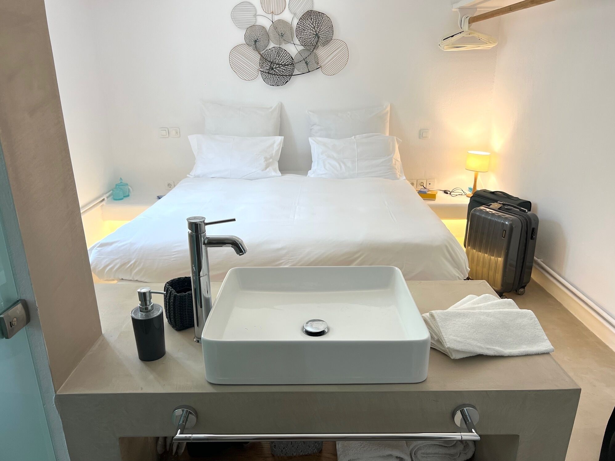 Een hotelkamer met een bed, een witte wastafel, een handdoek en een koffer.