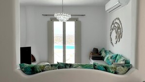 Ein Wohnzimmer mit einer gebogenen Couch, einem Chandelier und Meerblick durch ein großes Fenster.
