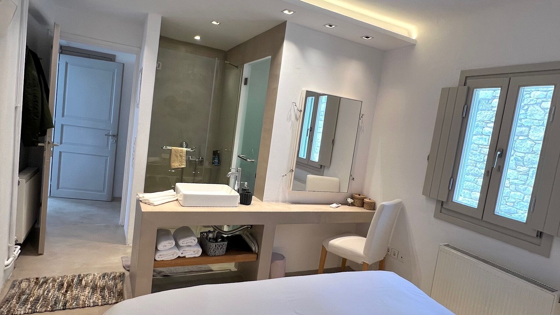 Ein modernes Hotelzimmer mit einem großen Bett, einem Schreibtisch mit Spüle, einem Spiegel und einer Dusche.
