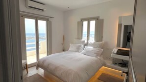 Ein Schlafzimmer mit Bett, Nachttisch, Spiegel und Meerblick durch große Fenster.