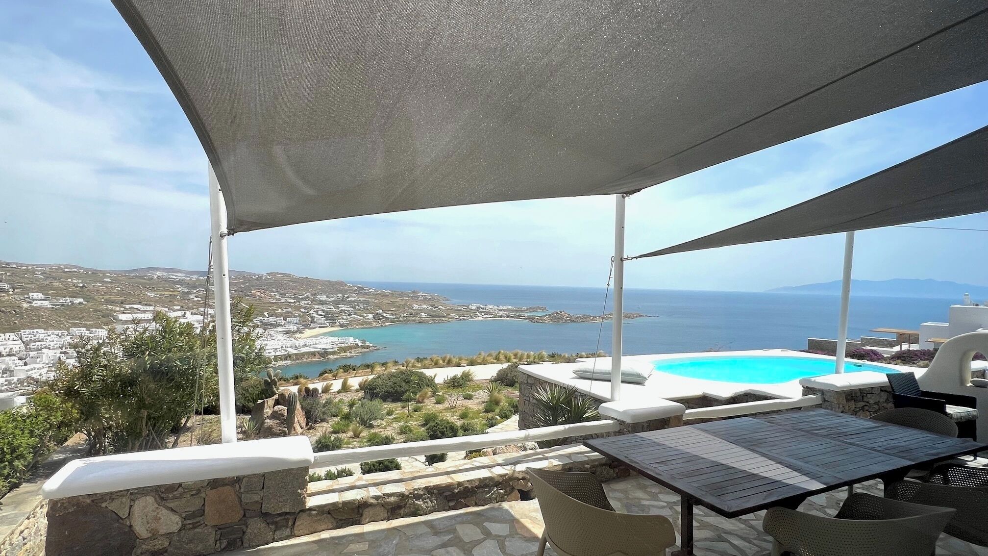 A terrace with a pool, outdoor seating, and a view of the sea and distant buildings.