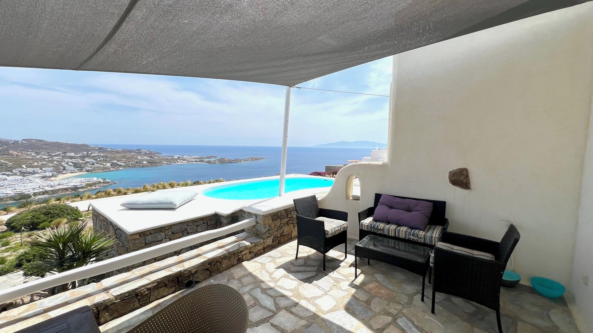 A terrace with a pool, outdoor furniture, and a view of the sea and town.