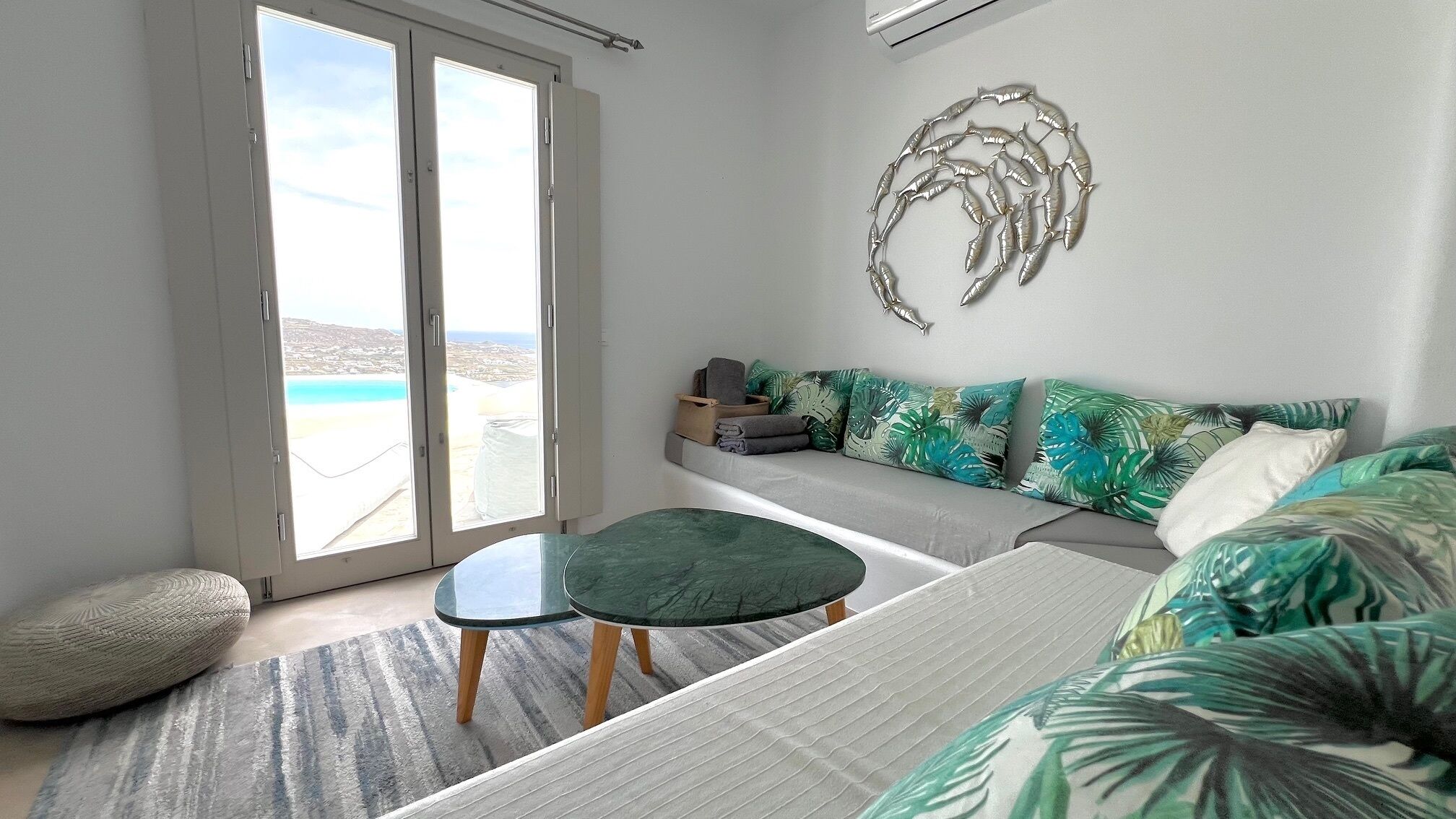 Un salon moderne avec un canapé, une petite table et une vue sur la mer grâce à de grandes portes coulissantes.