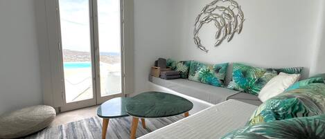 Un salon moderne avec un canapé, une petite table et une vue sur la mer grâce à de grandes portes coulissantes.