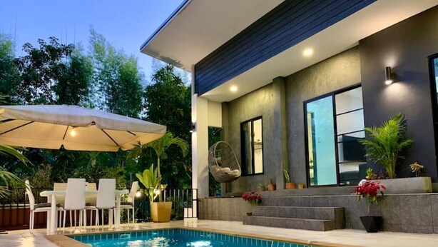 Ett modernt hus med en swimmingpool, utemöbler och krukväxter.