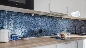 A modern kitchen with a blue mosaic backsplash, white cabinets, and a wooden countertop. - Comfortable Apartment in the Center | Balcony and Parking (Kolobrzeg)