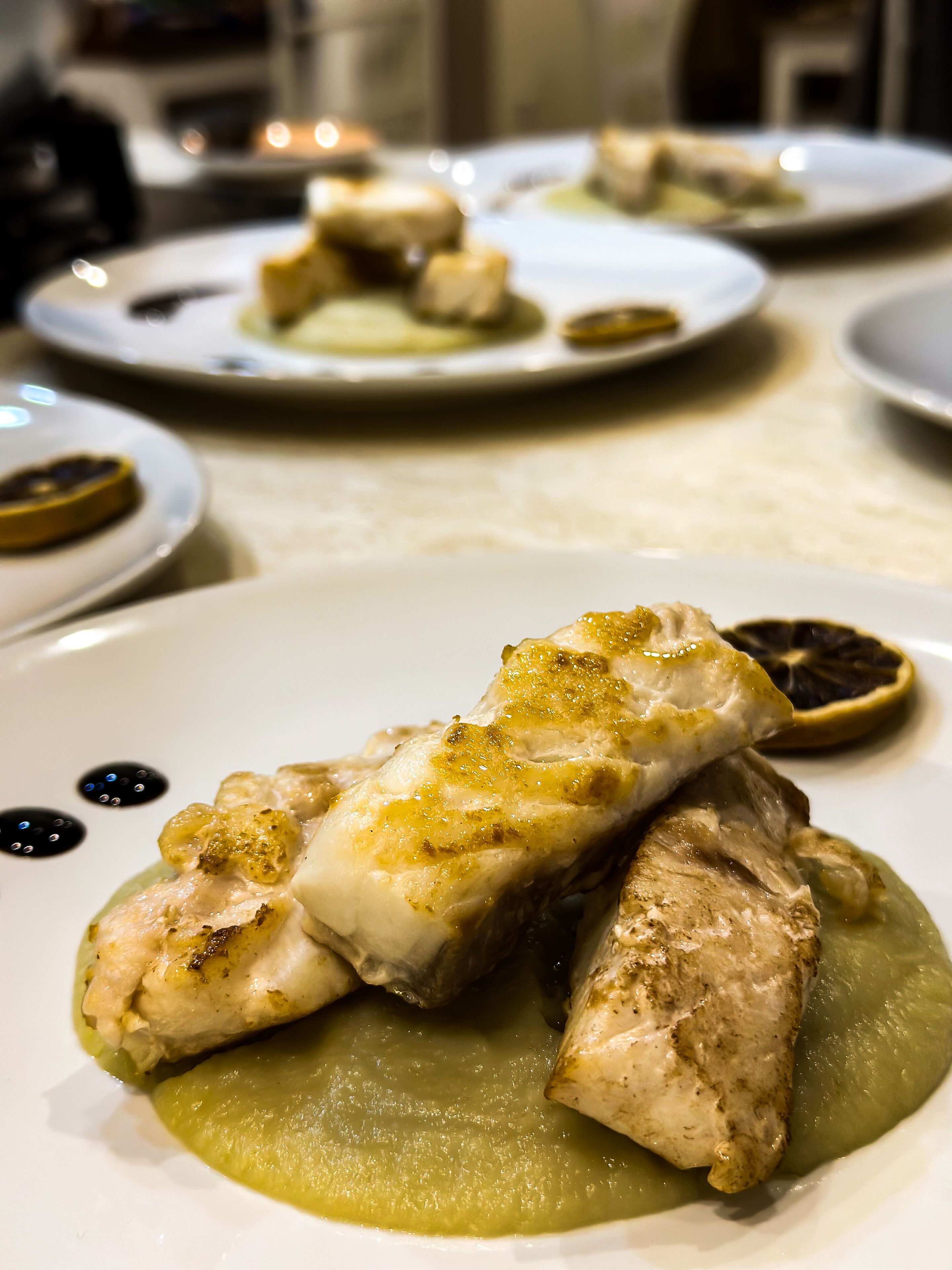A dining table with plates of food, including a piece of grilled fish and a green puree.