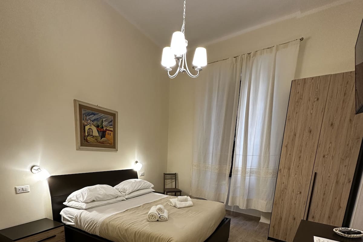 A modern bedroom with a large bed, bedside tables, a desk, and a hanging light fixture.