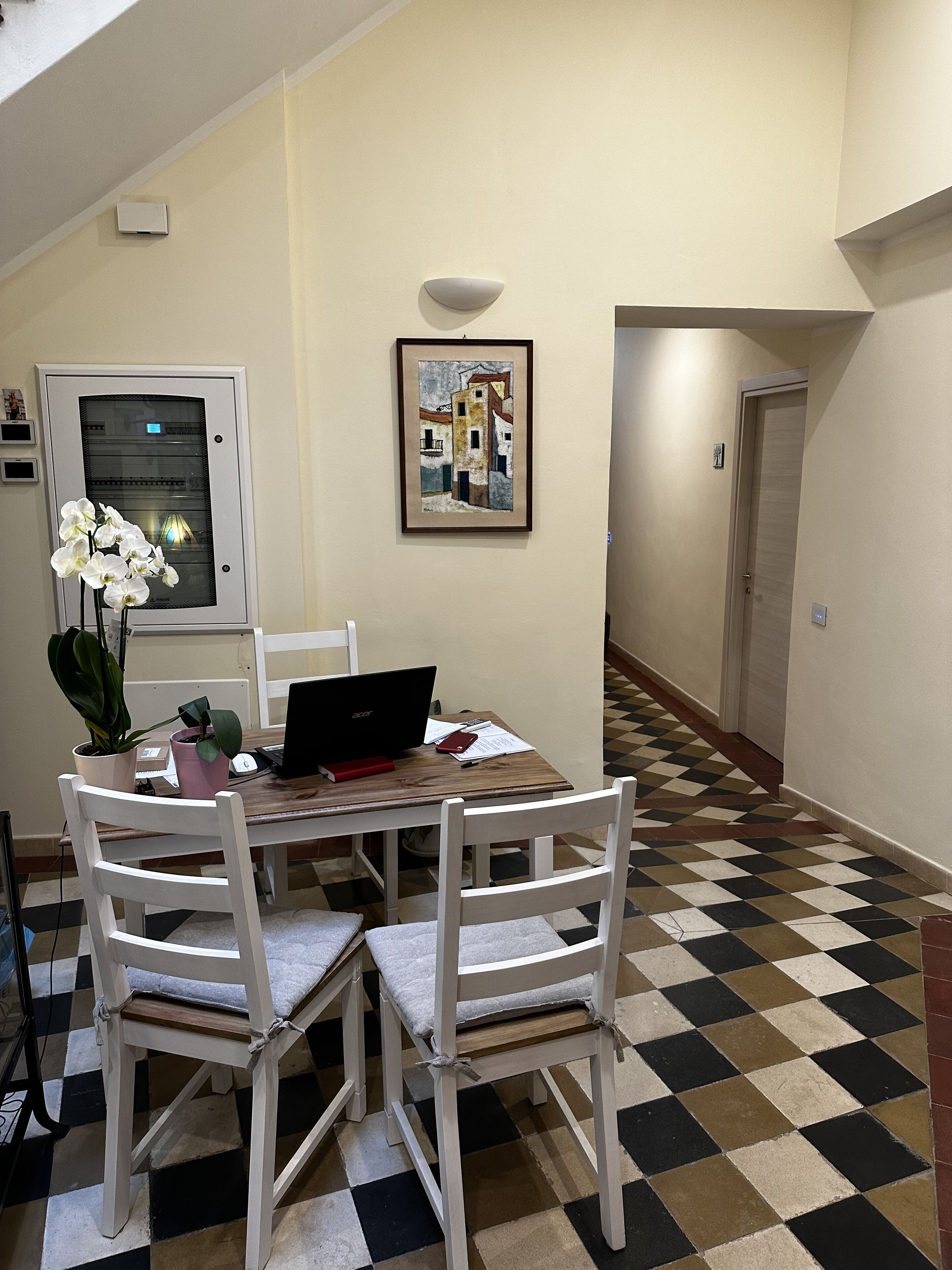 A dining area with a table, chairs, a laptop, and a framed artwork on the wall.