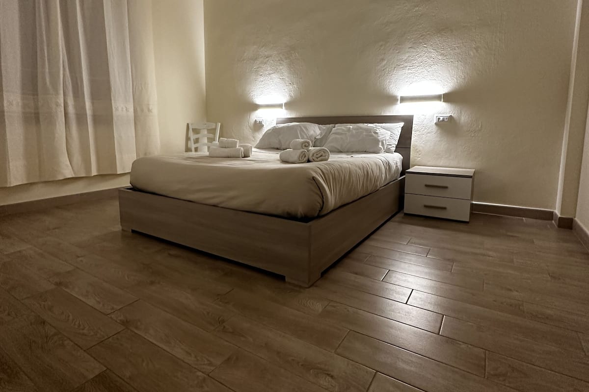 A bedroom with a bed, nightstands, a window with curtains, and a wooden floor.