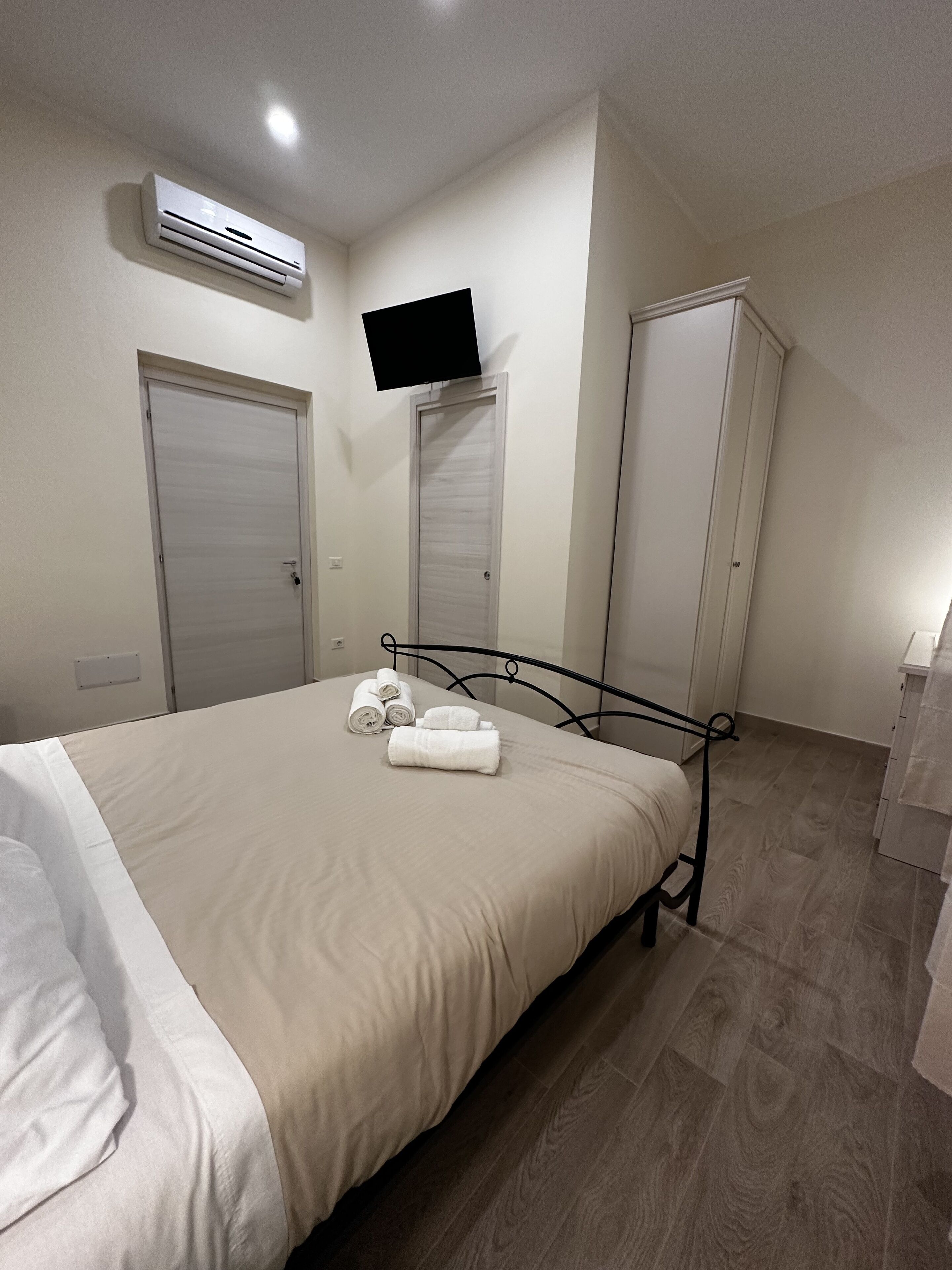 A bedroom with a bed, an air conditioning unit, a television mounted on the wall, and a wardrobe.