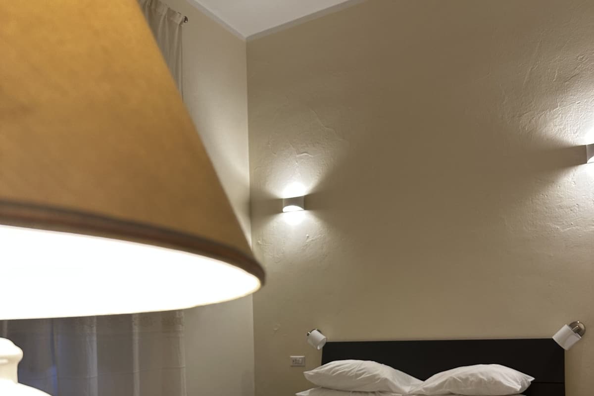 A neatly made bed with pillows and a rolled towel, a bedside table, and a lamp.