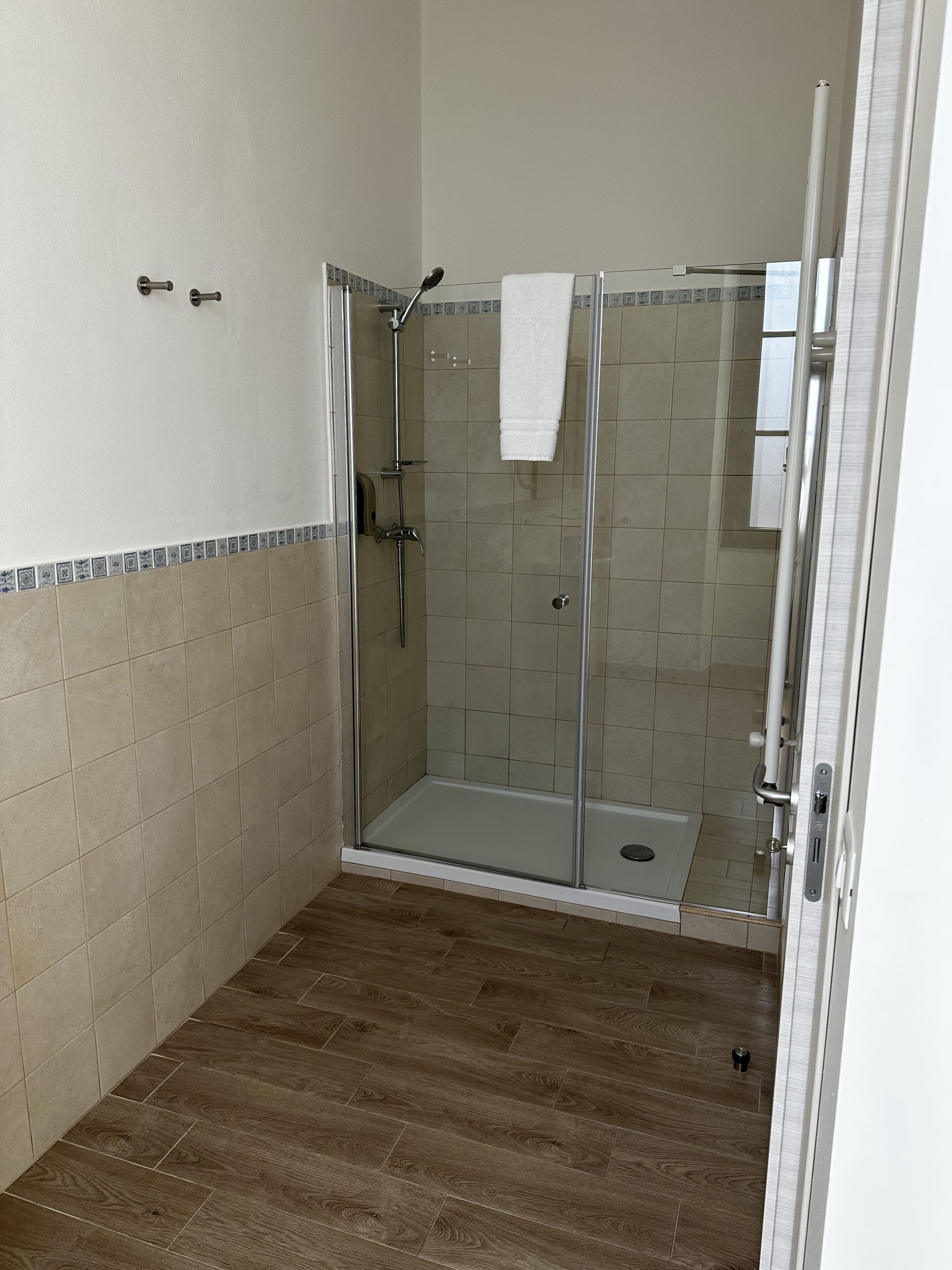 A glass-enclosed shower with a white towel hanging on the door, tiled walls, and a wooden floor.
