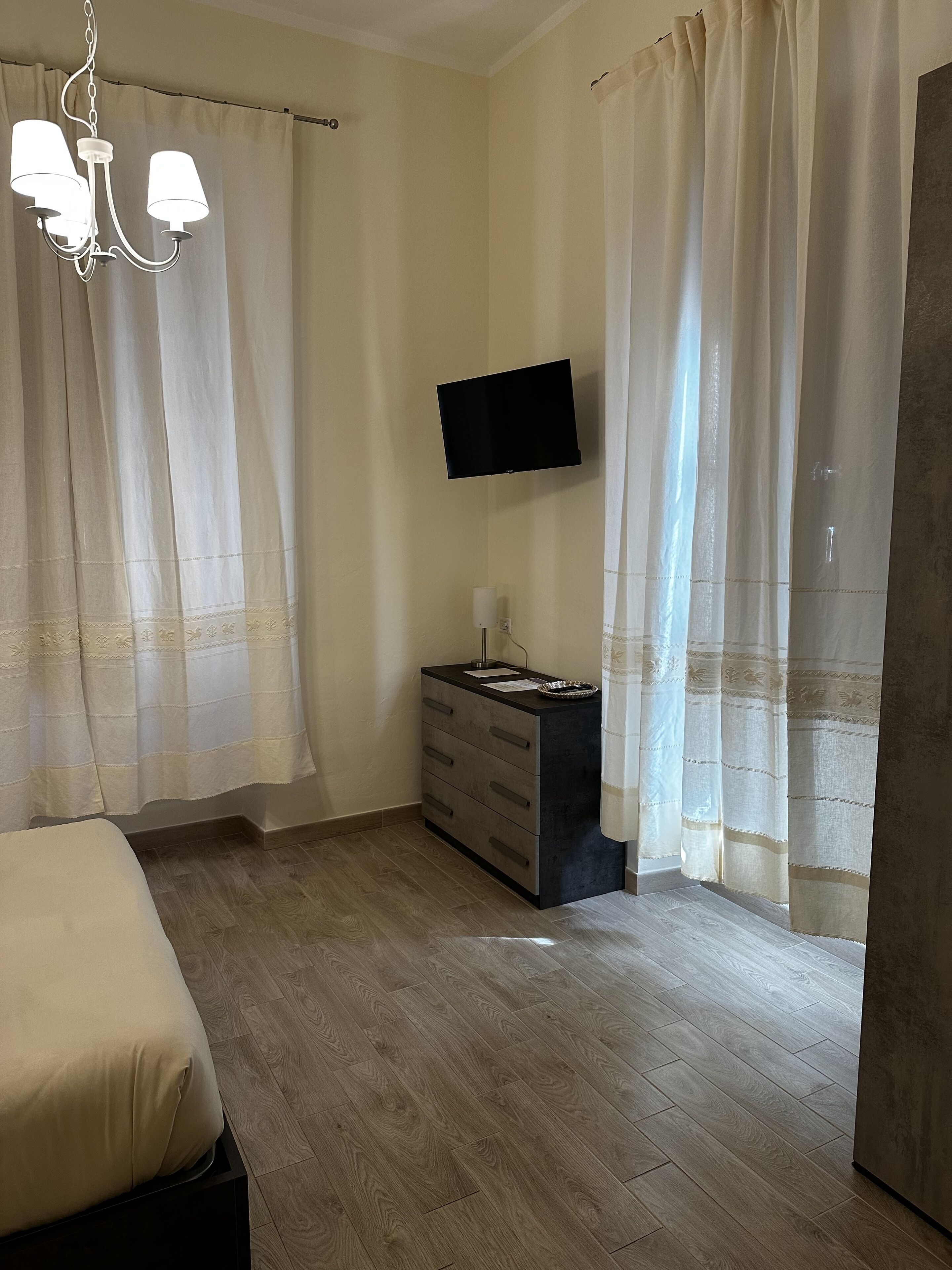 A bedroom with a bed, a dresser, a TV mounted on the wall, and a chandelier.
