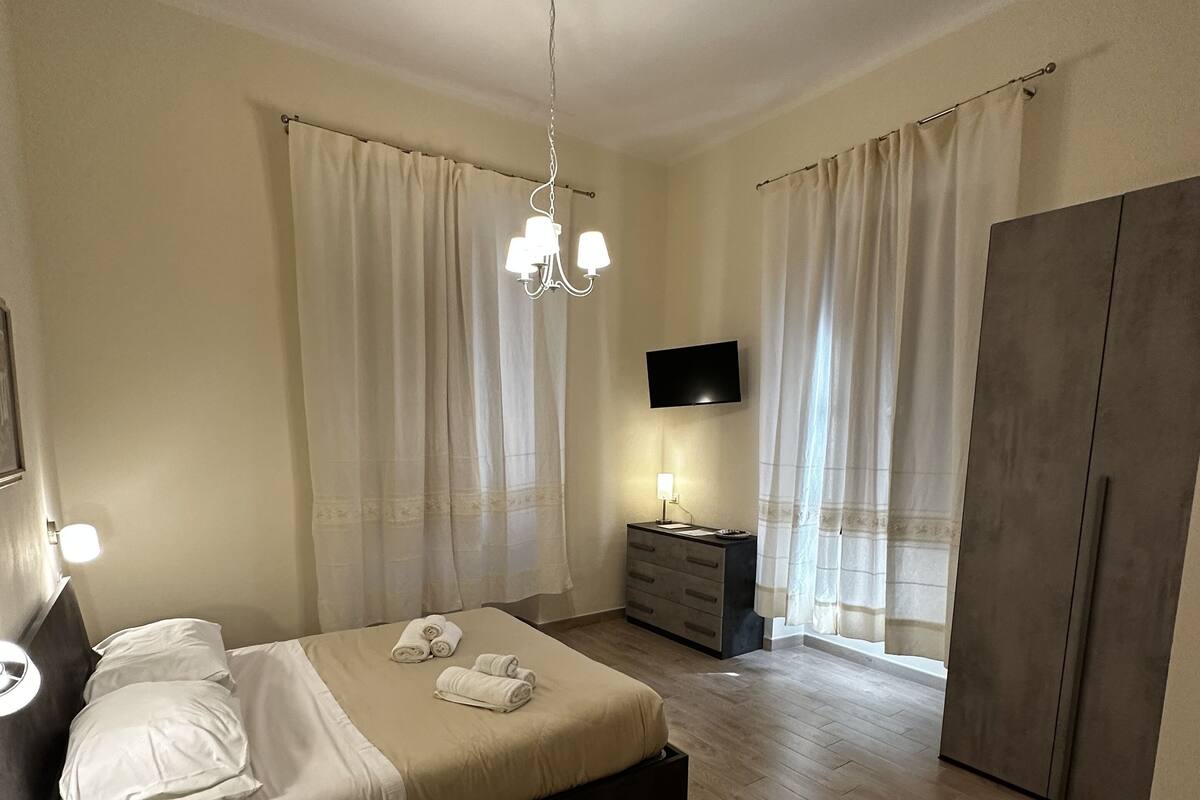 A modern bedroom with a bed, bedside table, dresser, and a TV mounted on the wall.