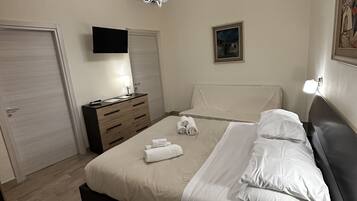 A bedroom with a bed, bedside tables, a TV, a painting, and a chandelier.