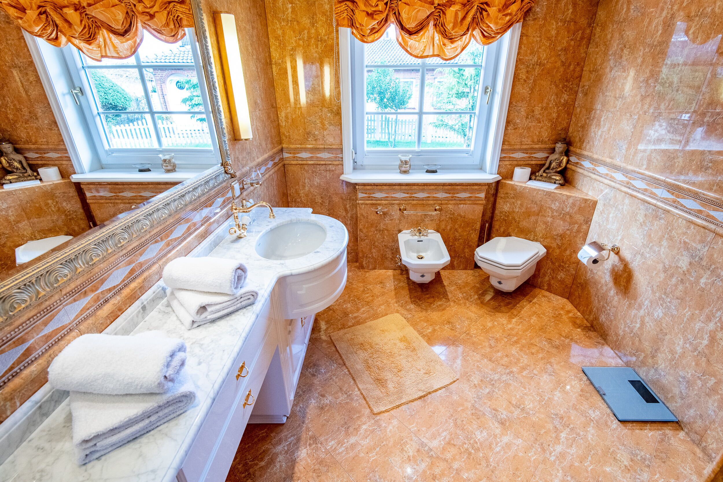 Ein luxuriöses Badezimmer mit Marmorboden, einem großen Waschbecken, zwei Toiletten und einem fenster mit Vorhängen.