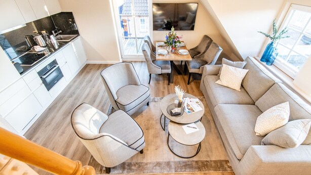 Una sala de estar moderna con un sofá, sillas, una mesa de centro y una mesa de comedor. Cuenta con una zona de cocina con estufa y armarios.