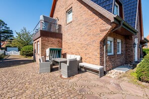 Un bâtiment en briques doté d’un balcon, d’un espace extérieur aménagé pour s’asseoir et d’une cour dallée.