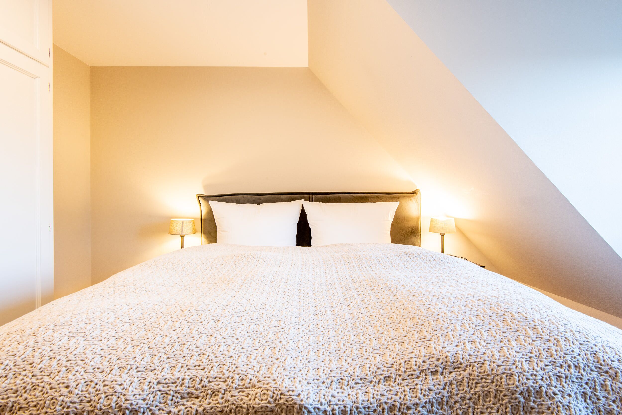 Una camera da letto con un letto grande, due lampade da comodino e un soffitto a falde.