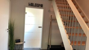 Ein modernes Interieur mit einer Holztreppe, einem Willkommensschild, einer Topfpflanze und einem kleinen Tisch mit einer Uhr.