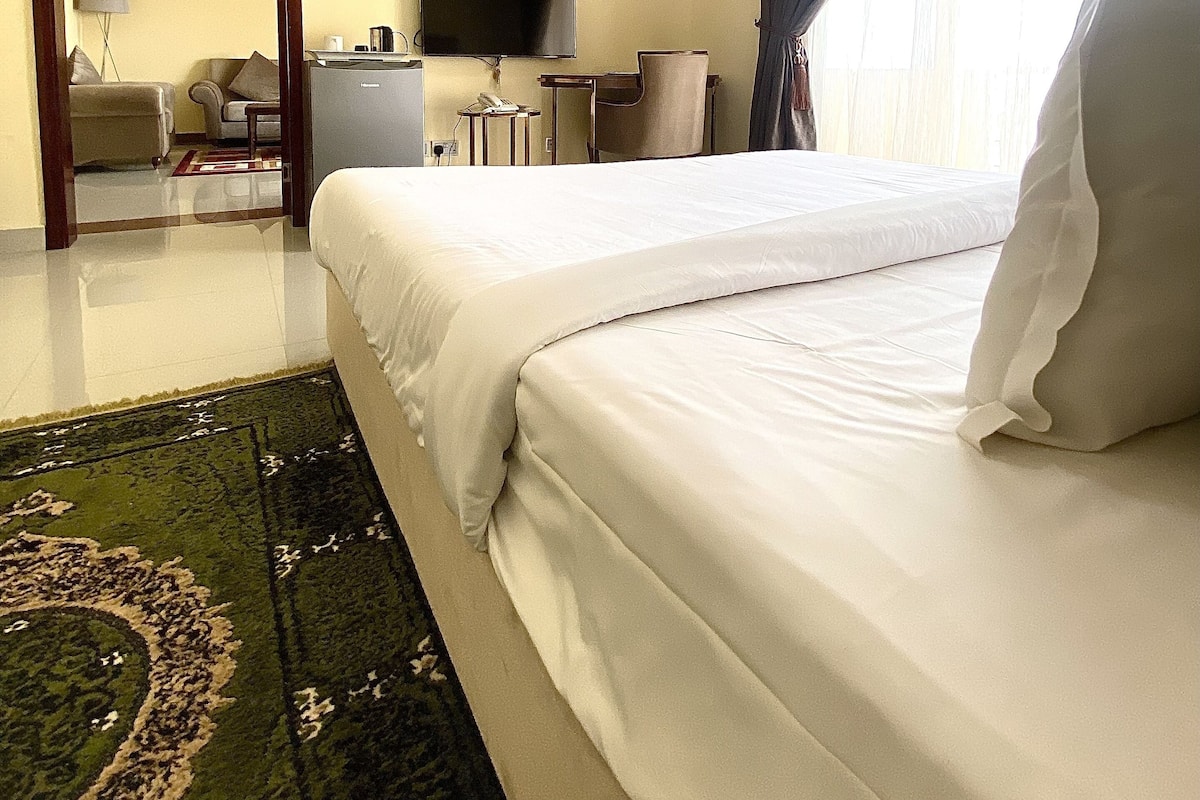 A hotel room with a bed, a desk, a chair, a TV, and an air conditioning unit.