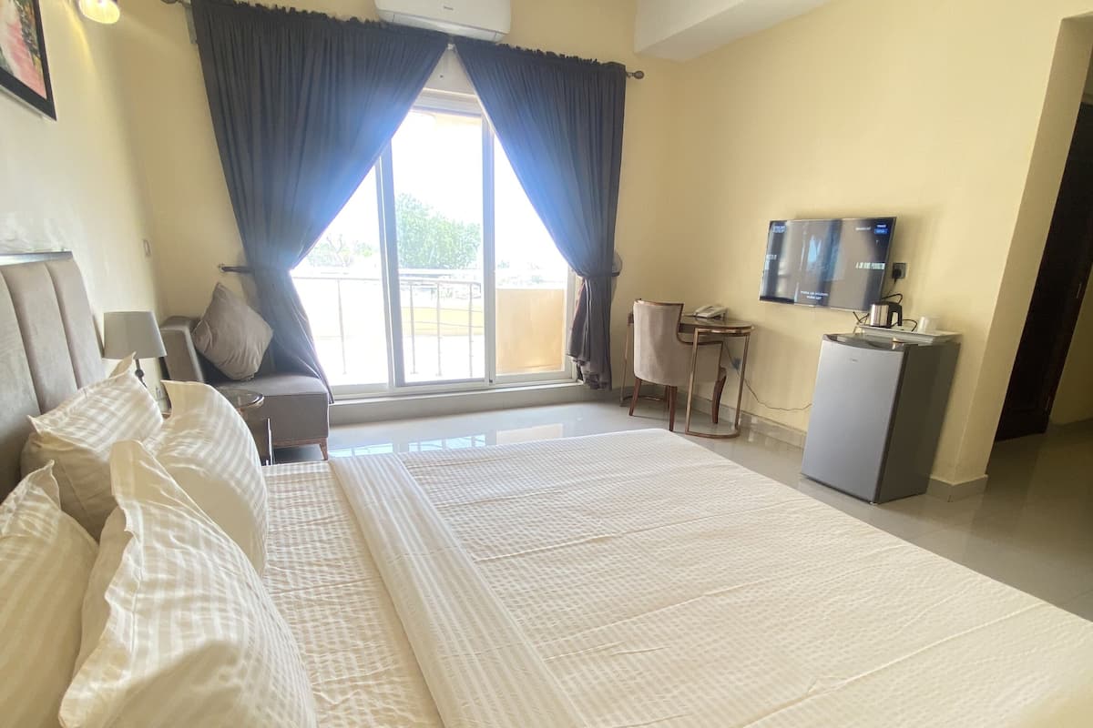 A hotel room with a large bed, a sofa, a desk with a computer, and a TV.