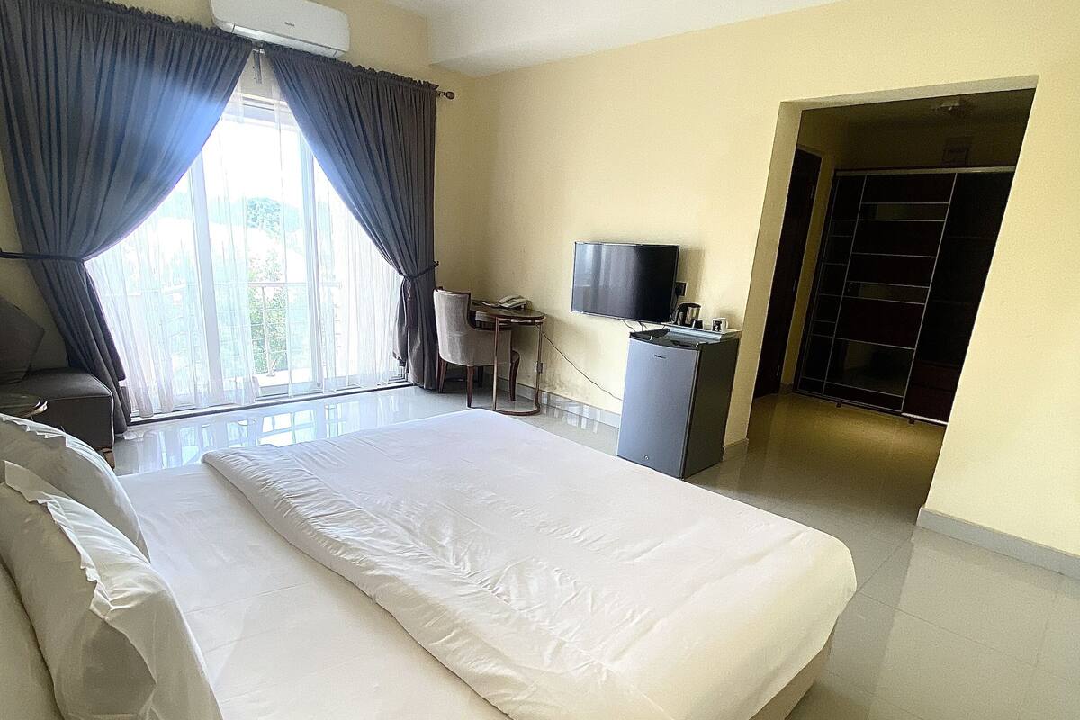A hotel room with a large bed, a desk with a computer, a television, and a wardrobe.