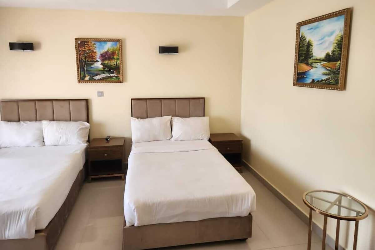 A hotel room with two beds, a small table, and two paintings on the walls.