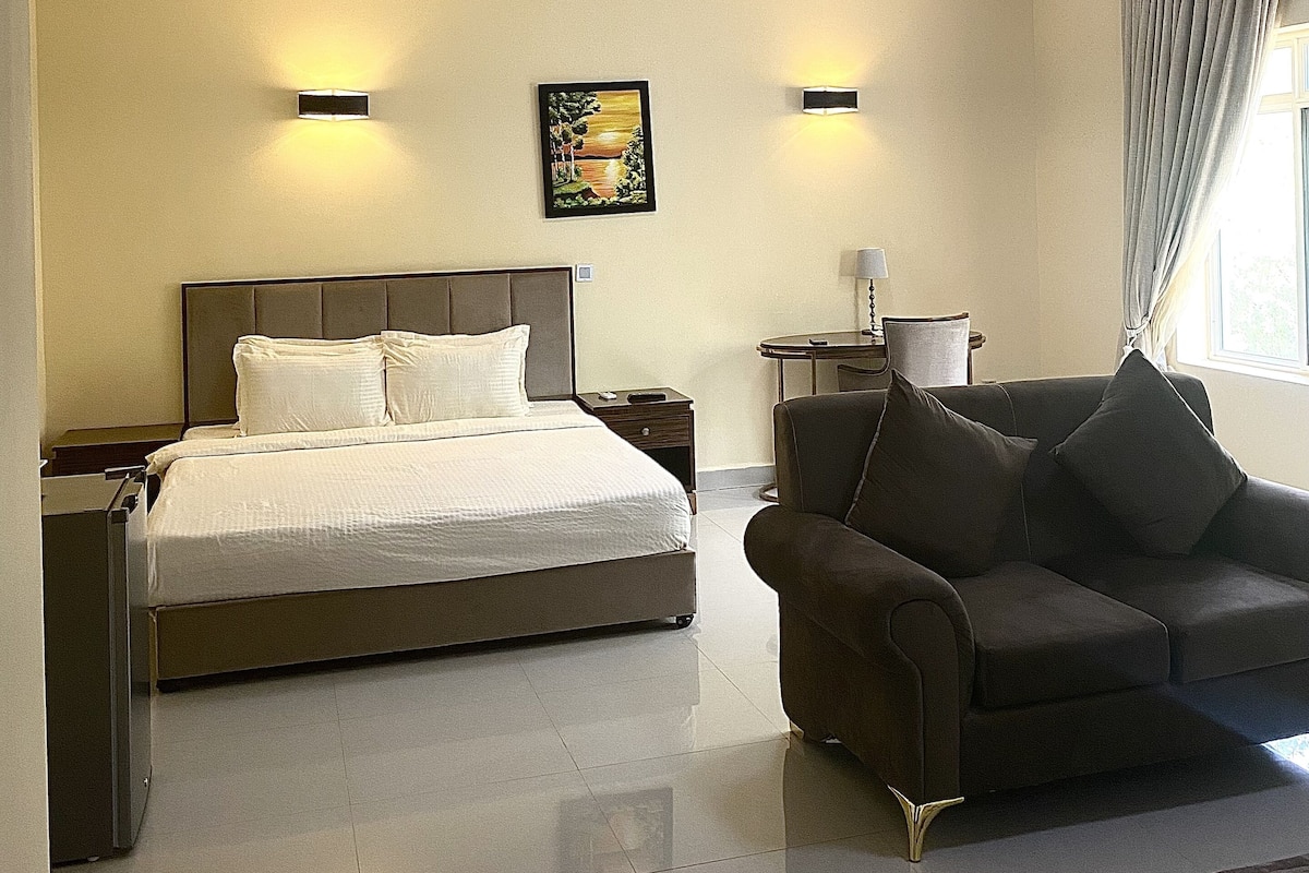 A hotel room with a bed, a sofa, a desk, and two wall-mounted lights.