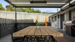 Une terrasse extérieure avec une table et des chaises en bois, un barbecue et un espace abrité offrant une vue sur le jardin arrière.