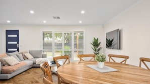 A modern living room with a wooden dining table, grey sofa, and a large window with blinds.