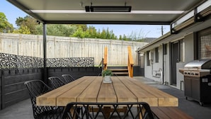 An outdoor patio with a wooden table and chairs, a grill, and a covered seating area.