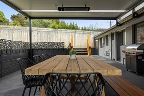 An outdoor patio with a wooden table and chairs, a grill, and a covered seating area.