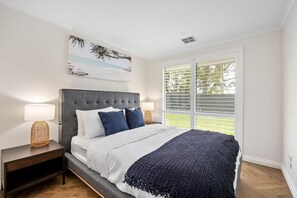 A bedroom with a large bed, two bedside lamps, a nightstand, a wall-mounted painting, and a window with blinds. - Secret Getaway, Capel Sound (Capel Sound)