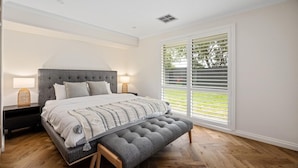 A bedroom with a large bed, a bench, a nightstand, and a window with blinds.
