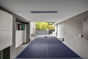 Ein Tischtennis-Tisch in einem modernen Innenraum mit einer Betonwand und einer Dartscheibe.