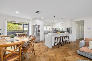 A modern kitchen with white cabinets, stainless steel appliances, and a central island with stools. - Secret Getaway, Capel Sound (Capel Sound)