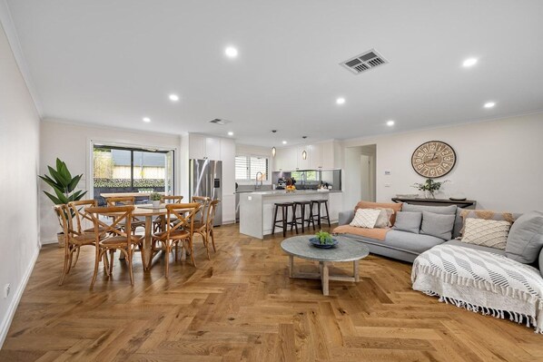 A modern living room with a dining area, kitchen, and a large window.