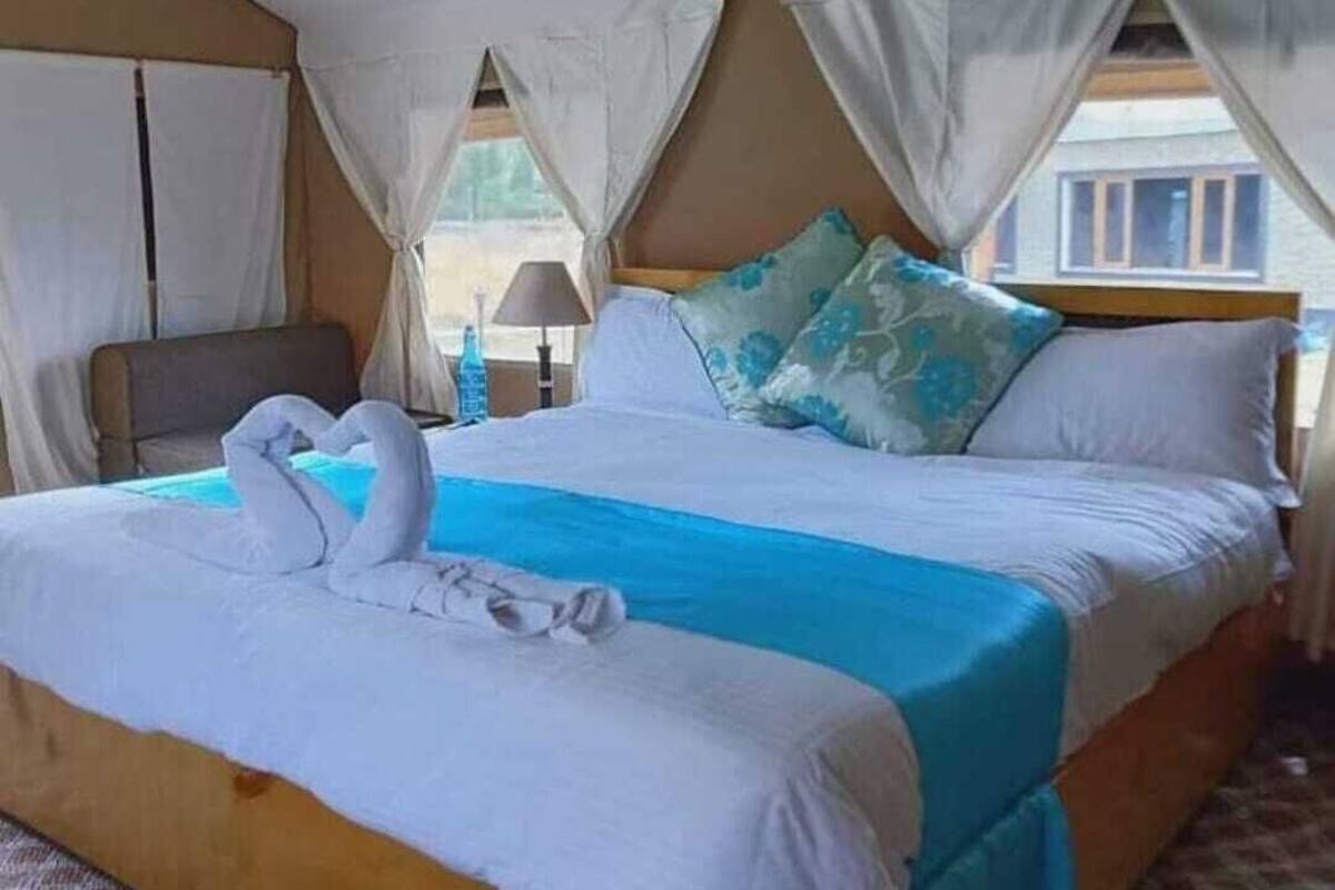 A bed with a blue bedspread, white pillows, and a swan-shaped towel arrangement.